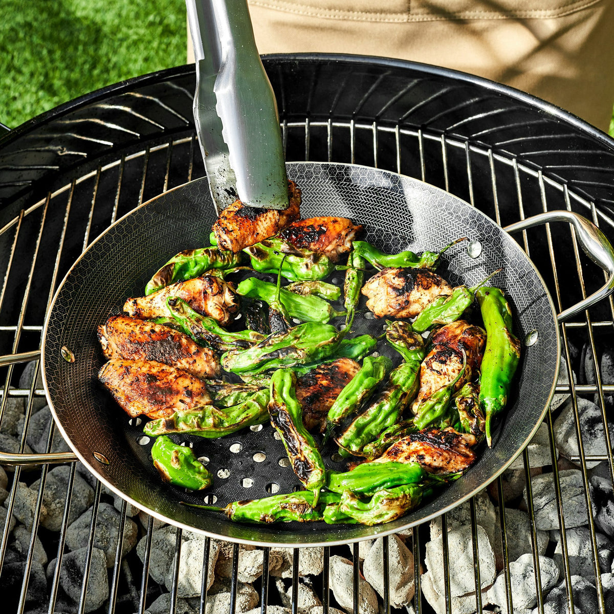 Chicken wings and green peppers being sauted in the HexClad 12&quot Hybrid BBQ Grill Pan on top of a grill